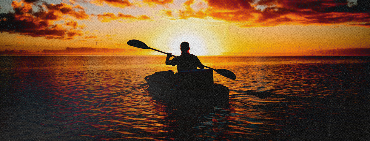 Silhouette of a person kayaking on calm water at sunset